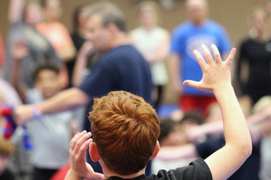 A red-haired camper with his hand raised to volunteer for the Prize Fight at Ken Chertow's summer wrestling camp