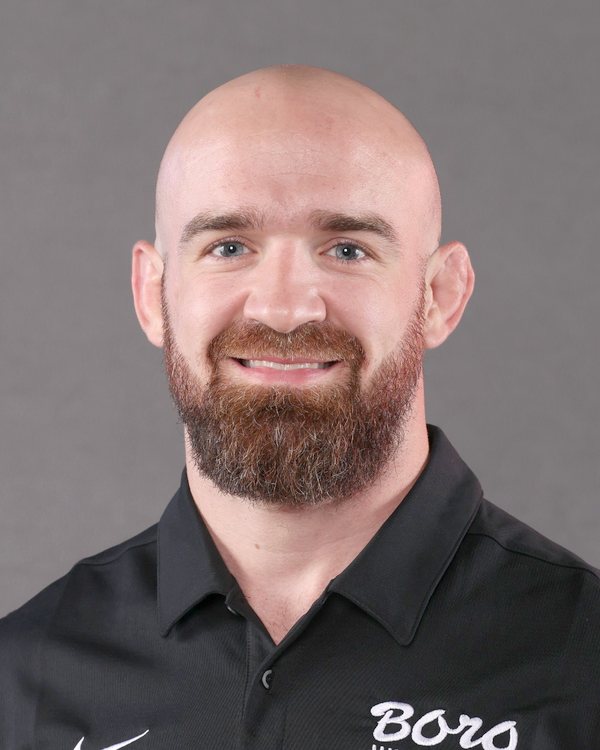AJ Schopp smiling in a black Boro Wrestling polo, Ken Chertow wrestling camp coach