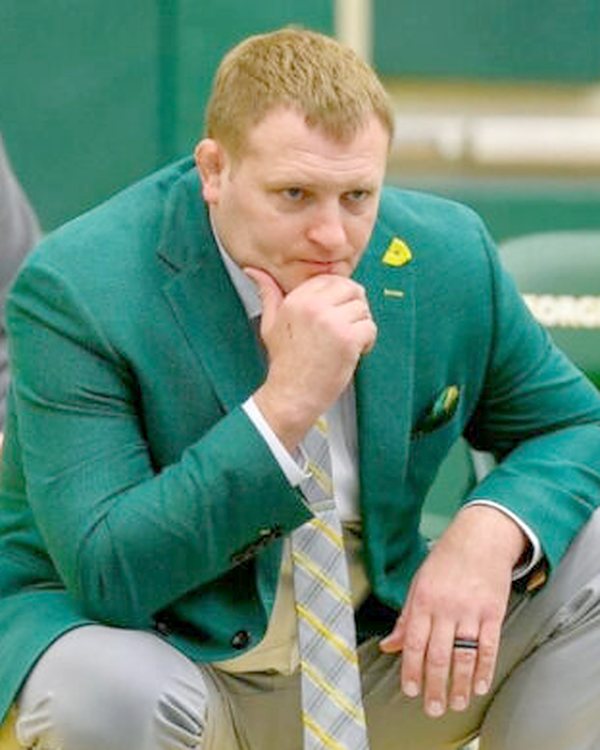 Frank Beasley crouching matside in a green blazer, chin resting on his hand, a Ken Chertow summer wrestling camp clinician