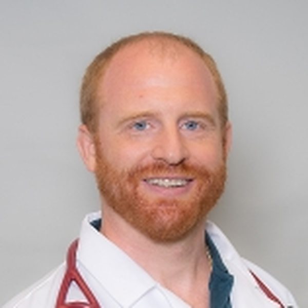 Jared Ricotta smiling in a white coat, Ken Chertow wrestling camp staff member