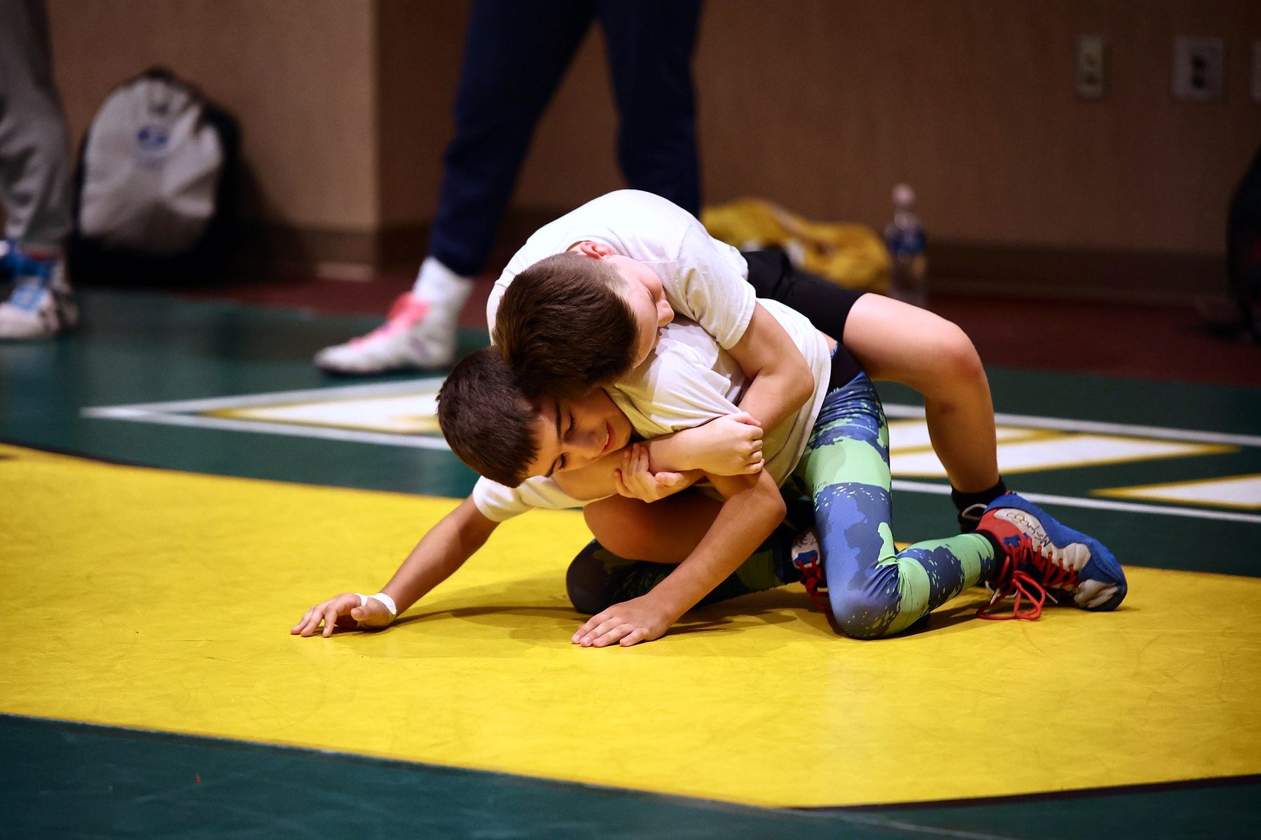 Two young wrestlers working a pin on the yellow mat at youth wrestling camp