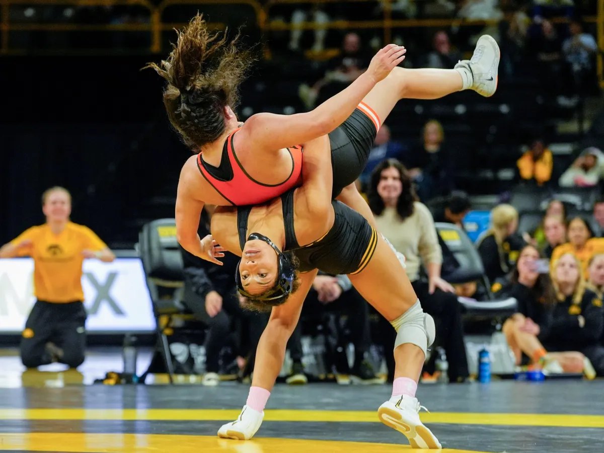 A women's college wrestler lifting her opponent off the mat for a throw in front of a crowd
