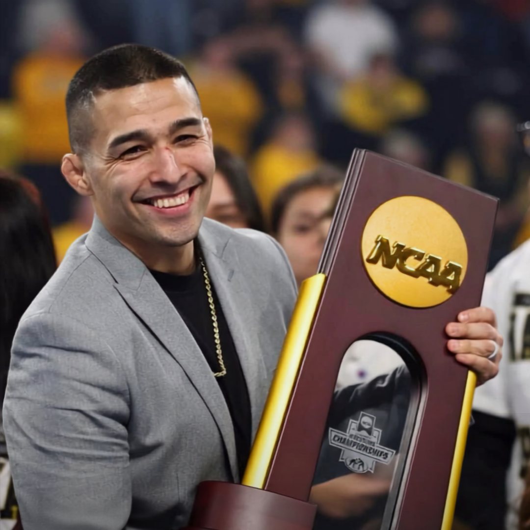 Alexio Garcia smiling and holding the NCAA championship trophy, SuperGirl girls wrestling summer camp coach