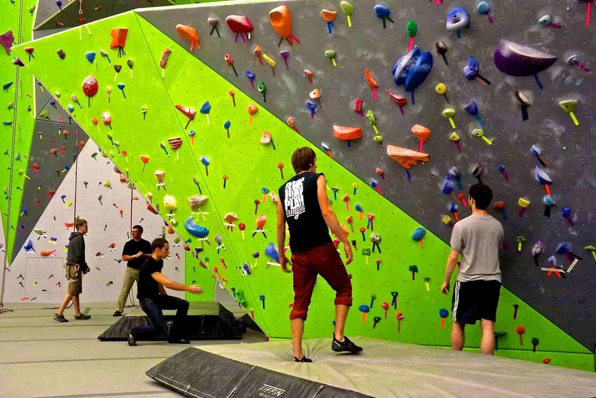 Climbers on a tall indoor climbing wall with bright green panels at Spooky Nook, home of SuperGirl girls wrestling camp